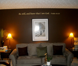 A Bible verse wall decal above the picture frame and a sofa with two lampshades on both sides in the living room - Be still and know that I'am God.